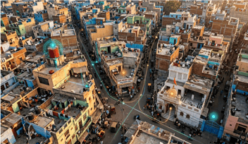 An aerial view of a dense urban neighbourhood with glowing digital route overlays connecting local landmarks like a red water tank, temple, and corner shop, illustrating AI-powered landmark-based address mapping for last-mile delivery.